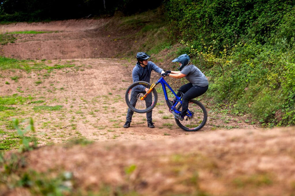 A man helping a woman on the bike by lifting up her front wheel and showing her how to balance